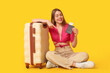 © Pixel-Shot - Beautiful young woman pointing at passport and suitcase on yellow background
