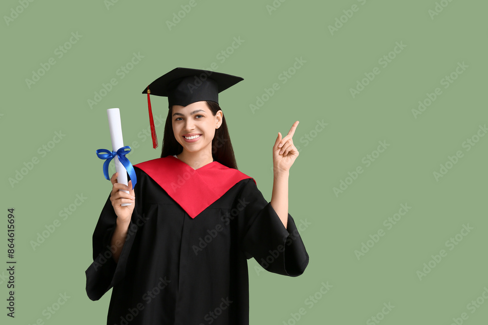 Happy female graduate with diploma pointing at something on green background