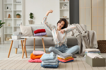 Poster - Young woman folding different clothes on floor at home