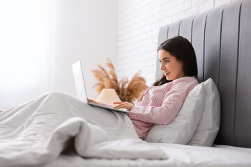 Wall Mural - Pretty young woman with laptop lying in cozy bed