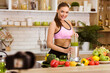 © Prostock-studio - A woman in athletic wear makes a green smoothie in her kitchen, with a variety of fruits and vegetables on the counter.