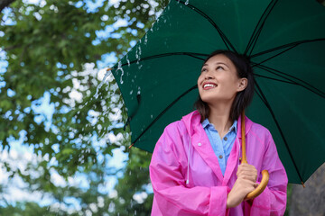 Poster - Portrait of young Asian woman man in raincoat holding umbrella outdoors on rainy day