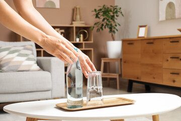 Wall Mural - Woman with bottle of water and glass on table at home, closeup