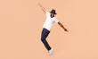 © Prostock-studio - A young black man in a white t-shirt and black fedora is dancing with his arms outstretched in front of a peach-colored background, panorama with copy space