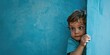 © Alexander Chaykin - A young boy leaning against a blue background with a calm and relaxed expression