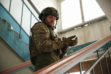 Wall Mural - Military mission. Soldier in uniform on stairs inside abandoned building, low angle view