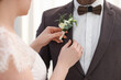© New Africa - Bride putting boutonniere on her groom's jacket against light background, closeup. Wedding accessory