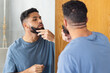 © Wavebreak Media - Grooming beard, man using comb and mirror for precise styling at home