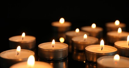 Wall Mural - Many burning tealight candles on black background, closeup