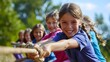 © dinny - Kids play tug of war in sunny park. Summer outdoor fun activity. Group of mixed race children pull rope in school sports day. Healthy outdoor game for little boy and girl.