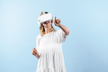 Wall Mural - Caucasian girl in pajamas enter in metaverse while point at blue background. Excited woman in white dress enjoy connecting in visual reality world program. Technology innovation concept. Contraption.
