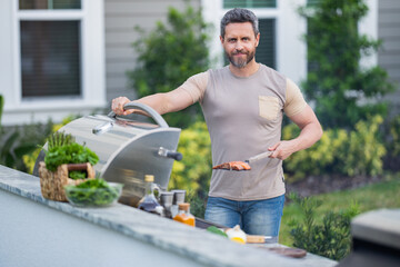 Poster - Man cooking tasty food on barbecue grill outdoors. Man cooking barbecue grill at backyard. Chef preparing food on barbecue. Millennial man grilling meat on barbecue grill. Bbq party. Meal grilling.