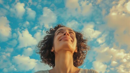Wall Mural - A woman with curly hair is smiling and looking up at the sky. The sky is blue with some clouds, and the woman's smile suggests that she is enjoying the beautiful day
