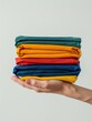 © Bendix - A Hand Holding A Stack Of Folded Colorful Fabrics In A White Room
