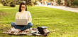 © Prostock-studio - Asian woman is sitting on a colorful blanket outdoors and using a laptop. She is focused on the screen, typing and scrolling. The setting appears to be a park or garden, panorama with copy space