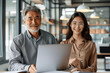 © btiger - Latin Manager Mentoring Young Asian Female Employee on Project Using Laptop in Office Team Setting
