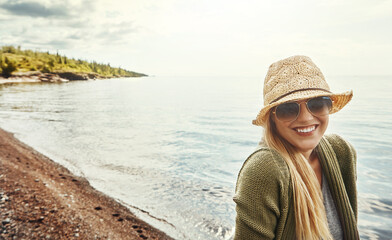 Happy woman, portrait and hat with glasses at beach for holiday, weekend or outdoor getaway. Young female person with smile in fashion for break, journey or trip in happiness by ocean coast in nature