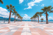 © Femmes.Digital - Geometric tiled walkway flanked by palm trees. Coastal promenade under a bright blue sky. Summer vibe.