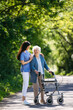 © Halfpoint - Female caregiver and senior woman with walker on walk in nature. Nurse and elderly woman enjoying a warm day in nursing home, public park.