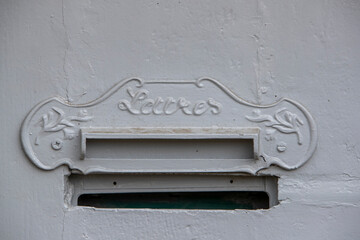 Détail d'une boite aux lettres de décor en fer forgé. Encastré dans un mur de couleur blanche.'Lettres' écrit en Français