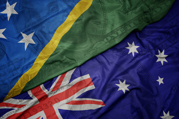Wall Mural - waving colorful flag of Solomon Islands and national flag of australia on the dollar money background. finance concept.