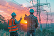 © Svetlana  - Two working engineers inspect electrical towers and power lines. The large suspended tower is visible against the clear blue sky at sunset.