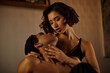 © LIGHTFIELD STUDIOS - A seductive Asian woman in black underwear embraces an African American man in a romantic and intimate moment on a bed.