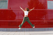 © VISTA by Westend61 - Cheerful woman jumping in front of red wall on sunny day