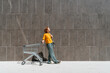 © VISTA by Westend61 - Woman standing with empty shopping cart near wall