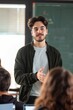 © siripimon2525 - 5. Portrait of an international student presenting a project in front of the class, bright lighting, confident expression, well-lit classroom