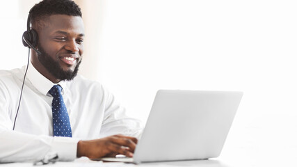 Young afro business consultant with headset typing email to client on laptop, empty space