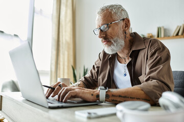 A mature gay man with tattoos and grey hair works from home, highlighting workplace diversity and LGBTQ+ inclusion.