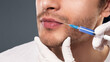 © Prostock-studio - Male lips close-up. Doctor inserting injection of hyaluronic acid in man's lips for treatment of wrinkles and facial rejuvenation, panorama