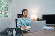 © itchaznong - Professional Woman Working from Home on Laptop with Headset in Modern Home Office Setting