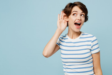 Wall Mural - Young curious nosy woman wears striped t-shirt casual clothes try to hear you overhear listening intently isolated on plain pastel light blue cyan color background studio portrait. Lifestyle concept.