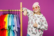 © ViDi Studio - Young lesbian woman wear pink animal clothes show colorful t-shirts wardrobe on rack at store show thumb up isolated on plain purple background studio portrait Pride day June month love LGBTQ concept