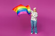 © ViDi Studio - Full body young fun happy lesbian woman wear pink animal clothes hold in hand waving rainbow striped flag isolated on plain purple background studio portrait. Pride day June month love LGBTQ concept.