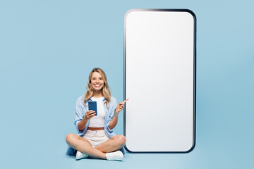 Wall Mural - Full body young happy woman wear white top shirt casual clothes point finger big huge blank screen mobile cell phone with area use smartphone isolated on plain blue cyan background. Lifestyle concept.