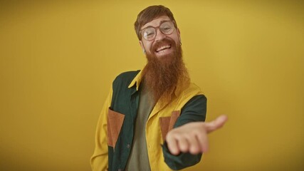 Canvas Print - Handsome young redhead man wearing glasses and shirt, standing over yellow background, offering friendly palm hand. sign of acceptance, giving help and assistance with a cheerful smile.