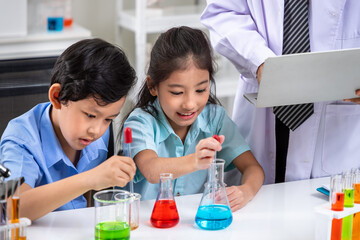 Asian pupils conducting colorful chemistry experiments under teacher's supervision in science lab