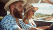 © BetterPhoto - A bearded man and a woman in hats driving a car on a sunny day. The man looks focused while the woman enjoys the ride, showcasing a relaxed summer road trip.