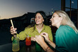 © Ilona - Two happy women sitting at a table in a bar drinking cocktails and chatting.