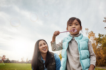 Mom, daughter and blowing bubbles in park with smile for fun, playing and bonding with child development. Asian parent, woman and happy with kid in garden on break for care, support and trust