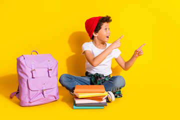 Wall Mural - Full size photo of small charming boy point look empty space backpack wear trendy white outfit isolated on yellow color background