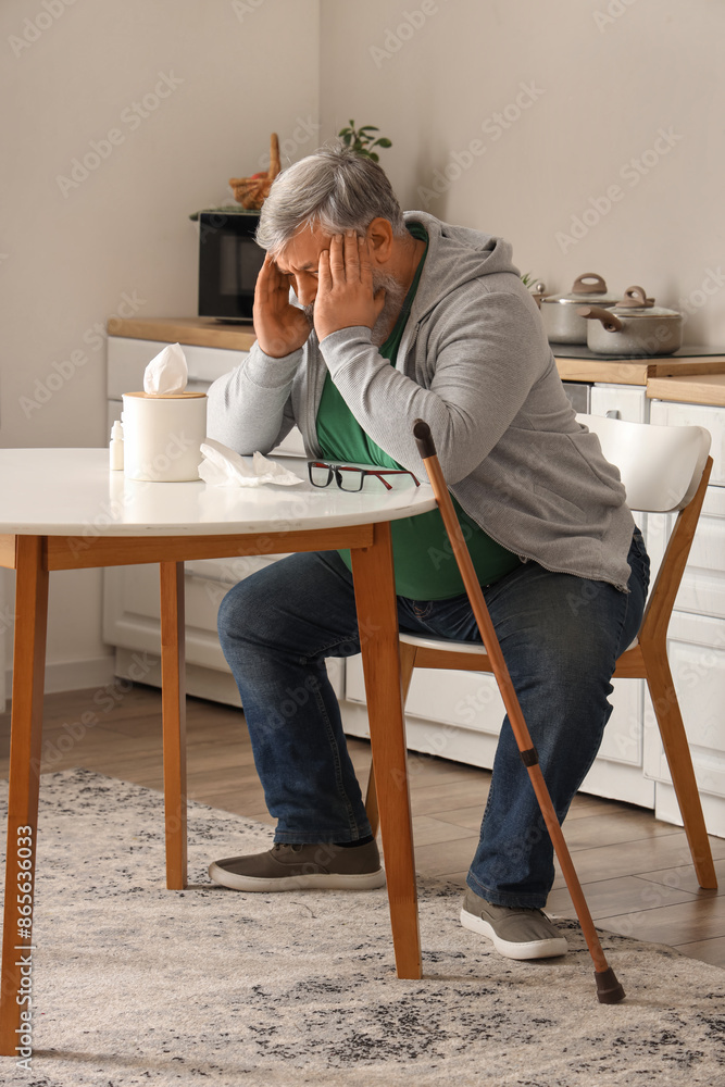 Portrait of sad senior man with tissues sitting at table in kitchen