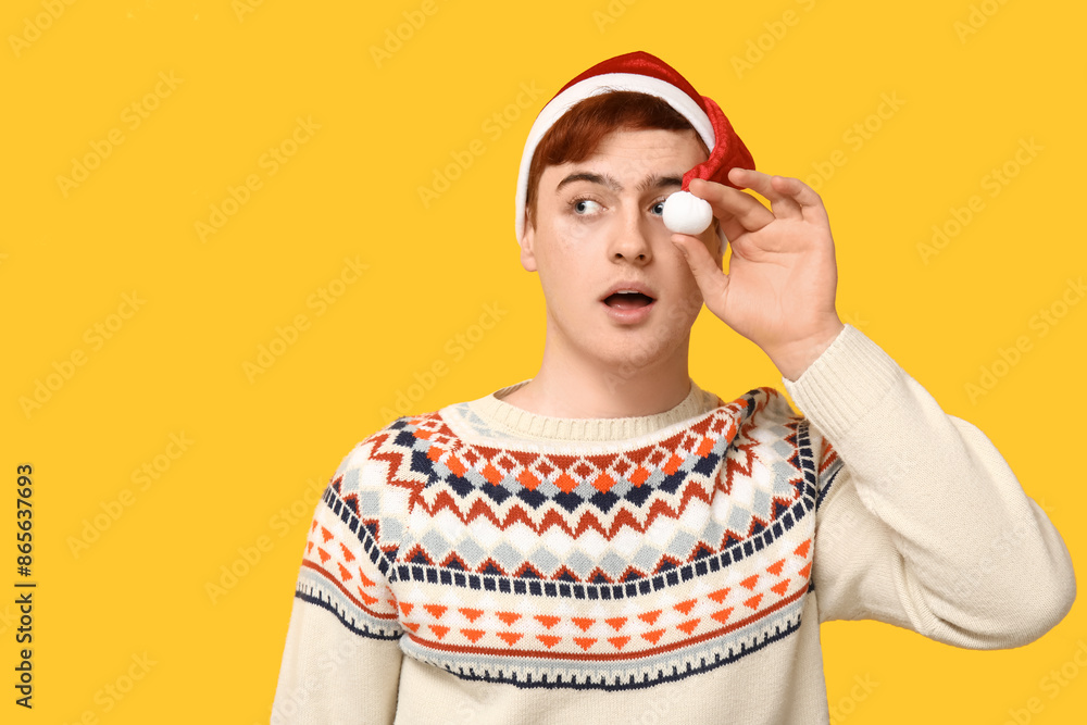 Surprised young man in warm sweater and Santa hat on yellow background