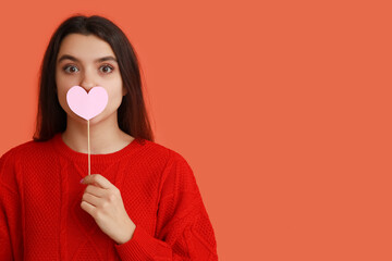 Wall Mural - Beautiful young girl with pink paper heart on orange background. Valentine's Day celebration