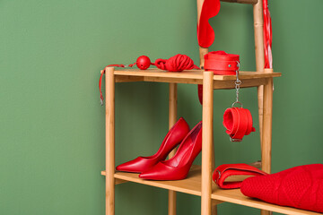 Wall Mural - Shelving unit with red sex toys and stylish female high-heeled shoes near green wall in room