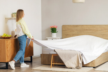 Poster - Pretty young woman making bed in bedroom