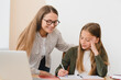 © InsideCreativeHouse - Young female tutor teacher babysitter nanny mother helping her daughter student pupil schoolgirl doing homework, explaining new topic at home.